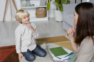 young woman doing speech therapy with little blonde boy young woman doing speech therapy with little blonde boy
